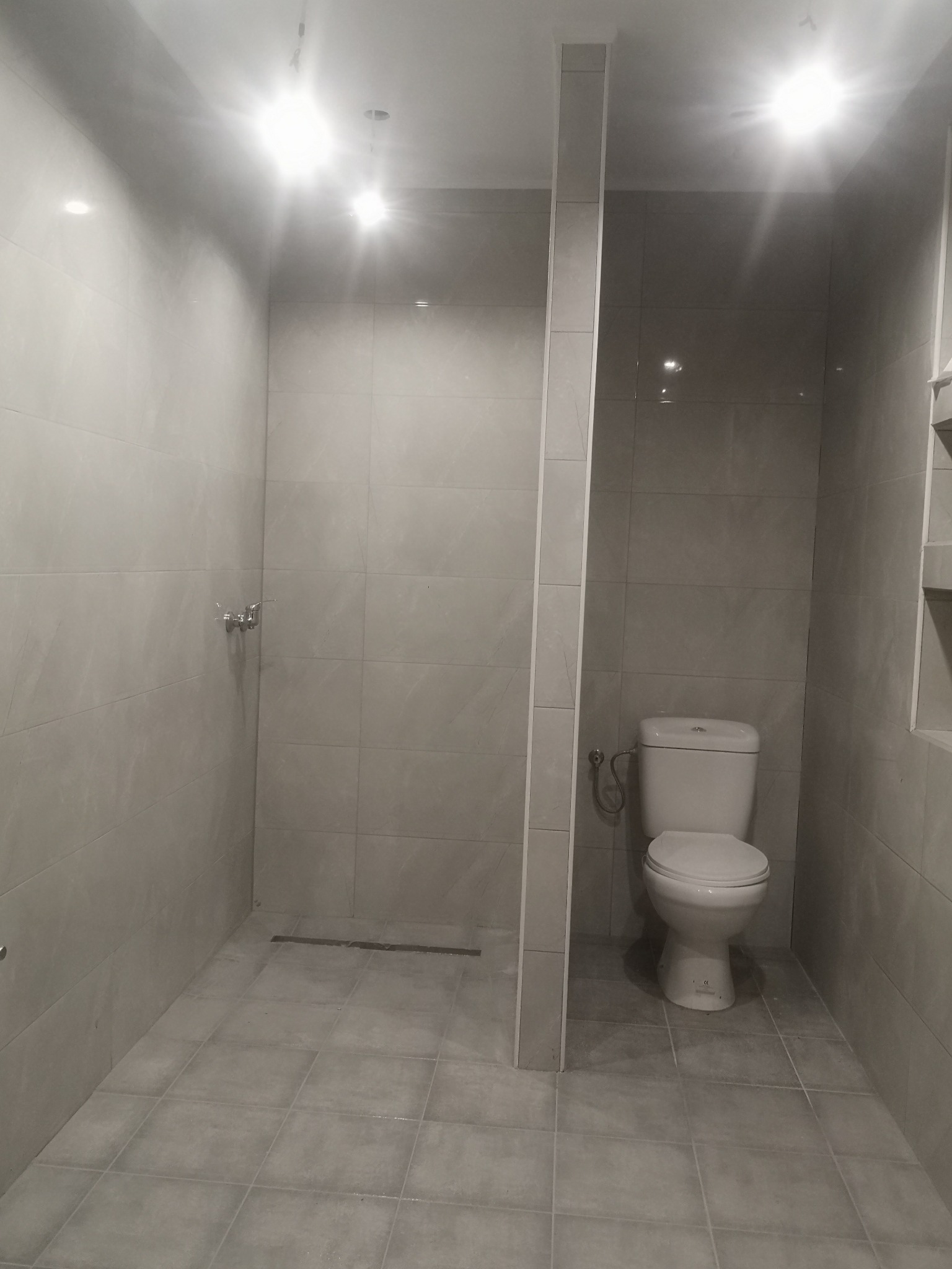 Wykończona łazienka z szarą glazurą, kabiną prysznicową typu walk-in i toaletą kompaktową, oświetlona punktowymi lampami sufitowymi.