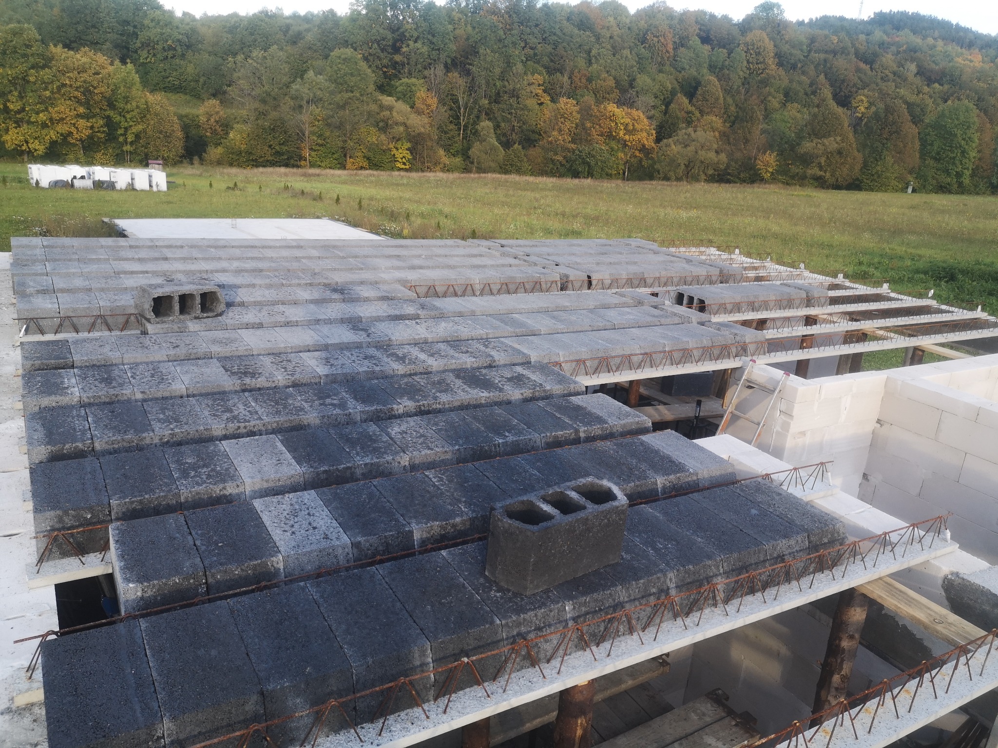 Wznoszenie stropu Teriva na budowie w Hoczewiu, widoczne pustaki stropowe i zbrojenie, w tle zielone drzewa.