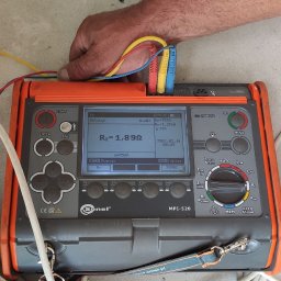 Karol Żurawski - Miernik Sonel MPI-520 w trakcie pomiaru rezystancji uziemienia, z widocznymi przewodami pomiarowymi w kolorach żółtym, czerwonym i niebieskim, oraz wyświetlonym wynikiem pomiaru.