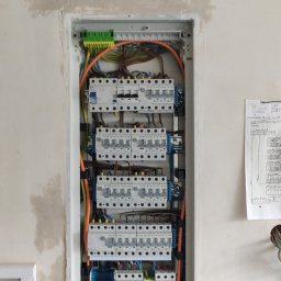 Karol Żurawski - Rozdzielnica elektryczna wnękowa z zamontowanymi bezpiecznikami, przewodami i listwami zaciskowymi, widok z przodu na tle ściany w trakcie wykończenia.