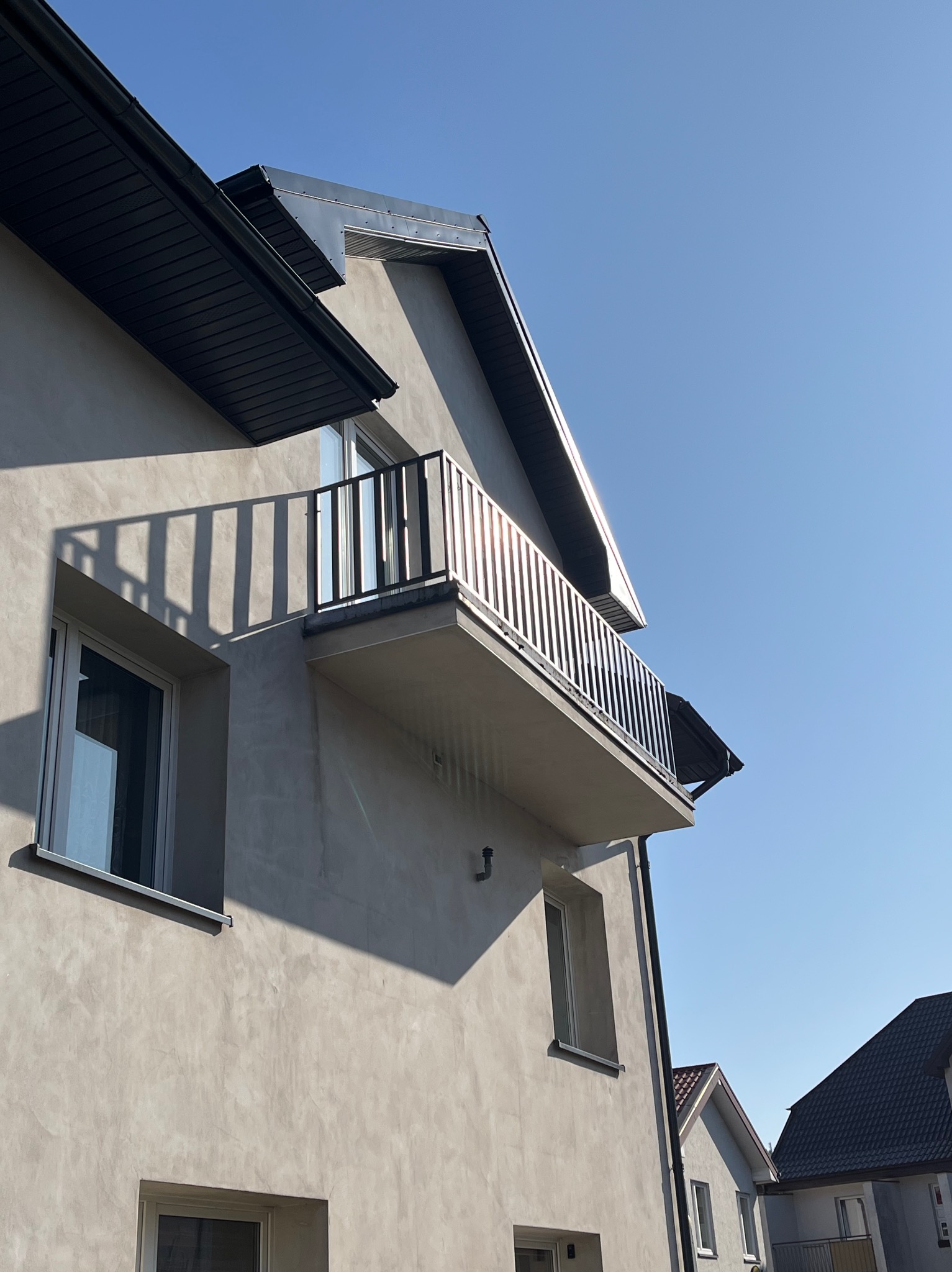 Nowoczesny balkon z metalową konstrukcją, widok z dołu na tle błękitnego nieba, rzucający cień na elewację budynku.