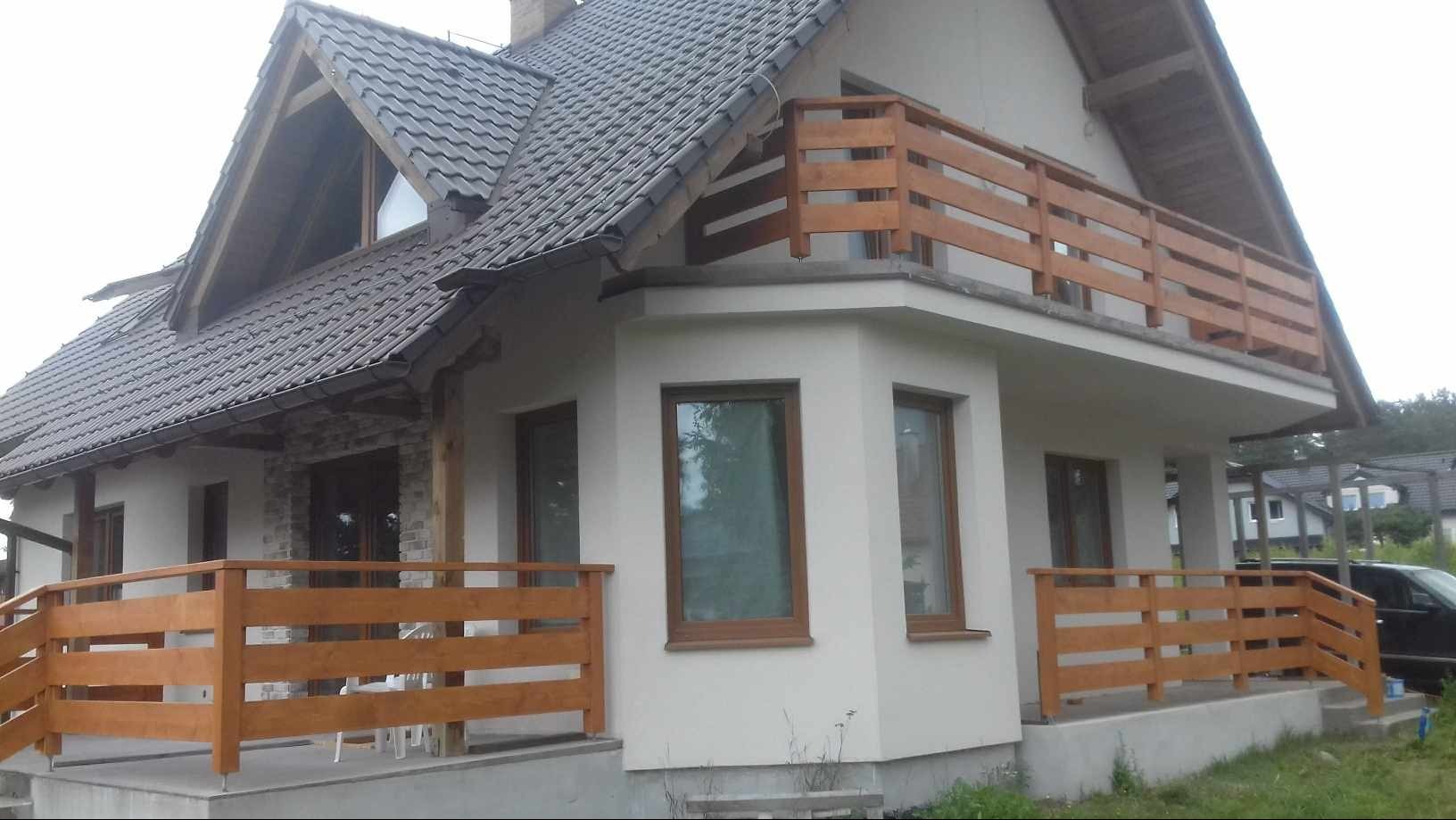 Nowoczesny dom jednorodzinny z drewnianą balustradą na balkonie i tarasie, widok z zewnątrz, szara dachówka, biała elewacja.