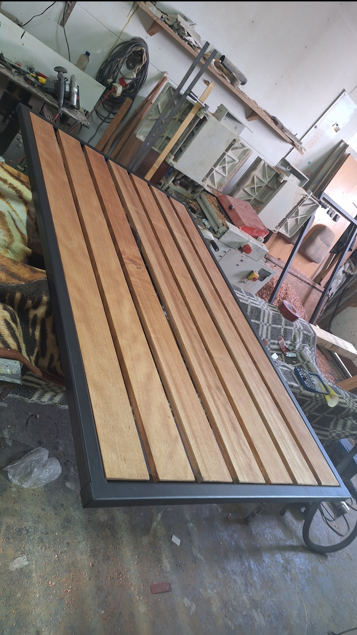 Drewniany taras z metalową ramą w warsztacie, widoczne deski i spawana konstrukcja. W tle narzędzia i materiały budowlane. Surowy, industrialny klimat.