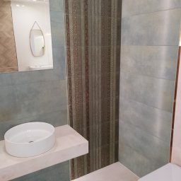 GRUPA FLEXIBLE SPÓŁKA Z OGRANICZONĄ ODPOWIEDZIALNOŚCIĄ - Nowoczesna łazienka z umywalką nablatową, lustrem z podświetleniem i dekoracyjnymi panelami ściennymi w odcieniach szarości i brązu.