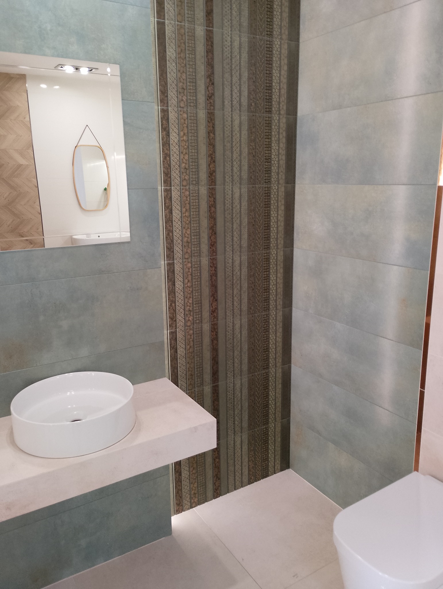 Nowoczesna łazienka z umywalką nablatową, lustrem z podświetleniem i dekoracyjnymi panelami ściennymi w odcieniach szarości i brązu.