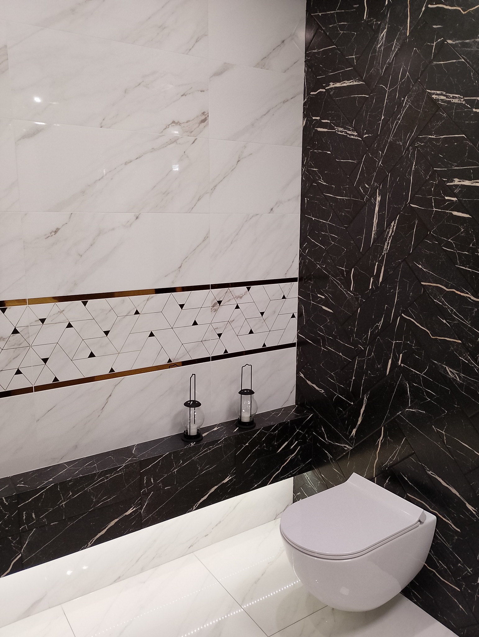 Nowoczesna łazienka z białymi marmurkowymi płytkami, pasem dekoracyjnym z geometrycznym wzorem i czarną ścianą z płytek imitujących marmur ułożonych w jodełkę, podświetlona listwa LED pod blatem...