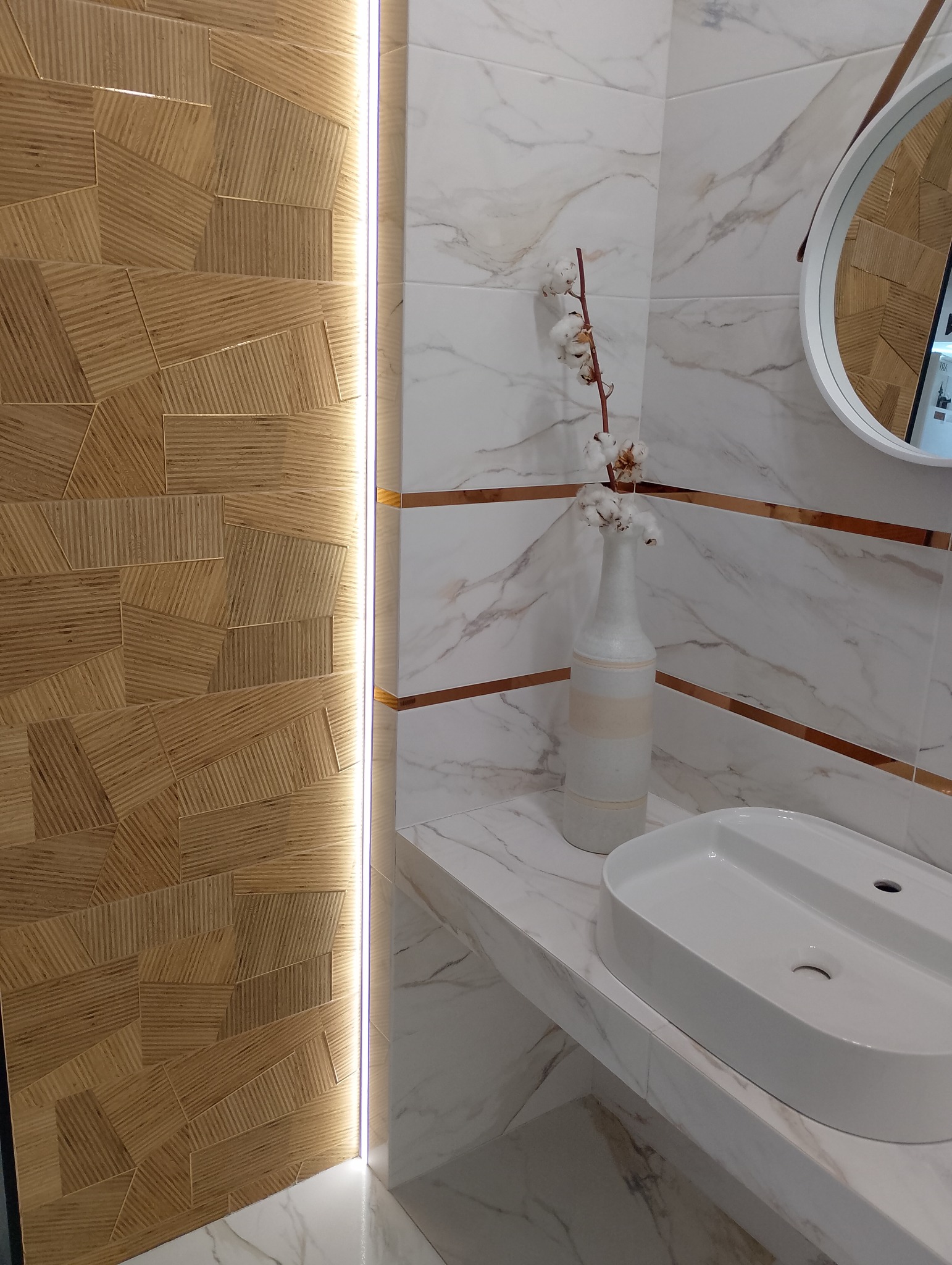 Nowoczesna łazienka z umywalką nablatową, drewnopodobną ścianą z podświetleniem LED i marmurowymi płytkami z dekoracyjnymi listwami, uzupełniona wazonem z bawełną.