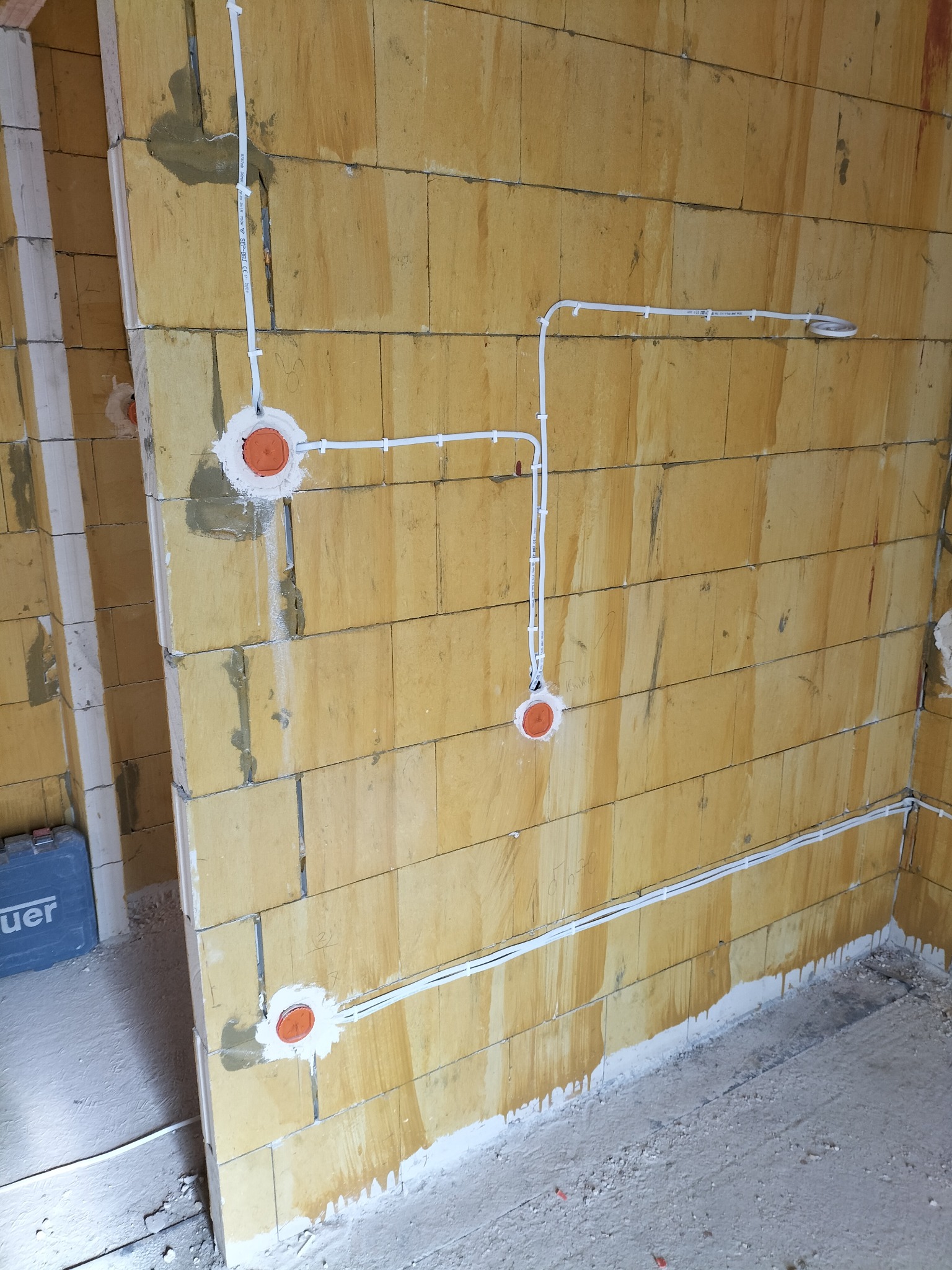 Instalacja elektryczna w trakcie montażu w nowym budynku w Łodzi. Widoczne kable prowadzone po ścianie z pustaków oraz puszki podtynkowe zamontowane w ścianie.