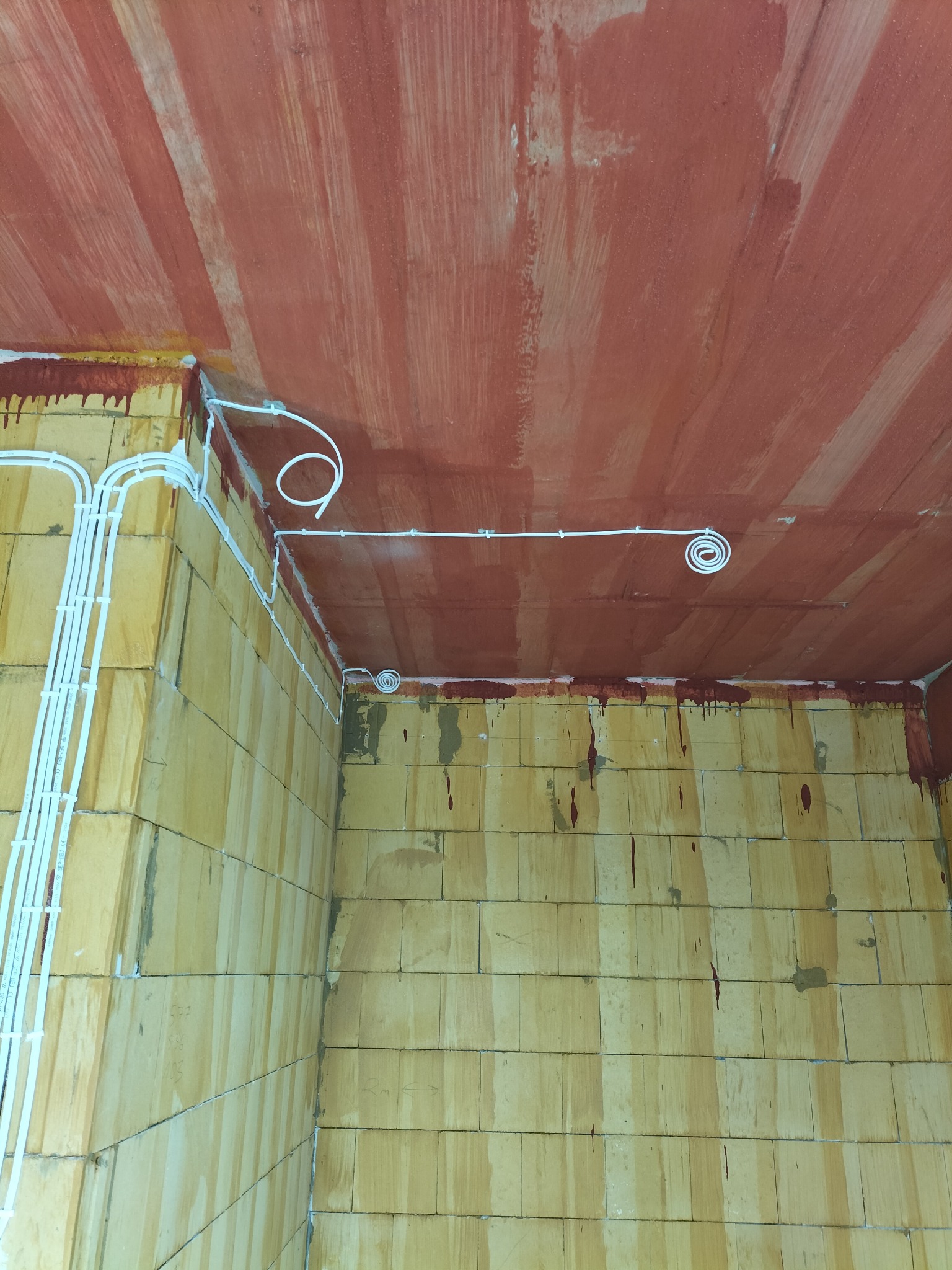 Surowy stan: Instalacja elektryczna natynkowa z białymi przewodami na ścianach z cegły i czerwonym, malowanym suficie w trakcie budowy.