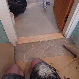 MAR-BUD CONSTRUCTION - Montaż drewnianego progu w odnawianej łazience z turkusowymi płytkami, widoczny aplikator do silikonu i zabezpieczenia podłogi.