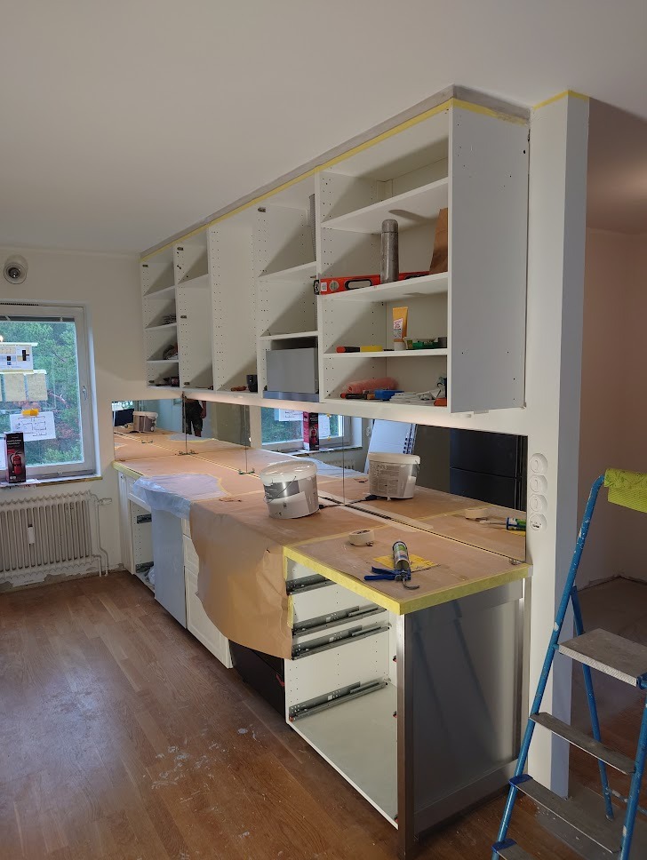 Montaż zabudowy kuchennej z otwartymi szufladami, zabezpieczonym blatem i górnymi szafkami w trakcie instalacji.