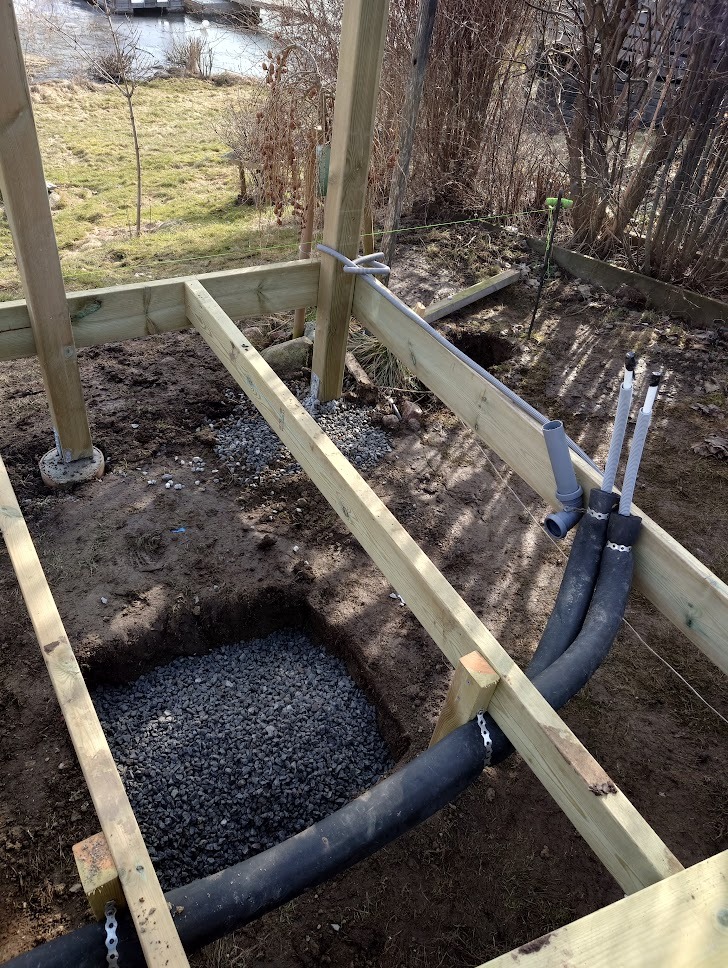 Konstrukcja drewniana w trakcie budowy na ziemi z widocznymi instalacjami, podsypką z kamienia i elementami mocującymi.