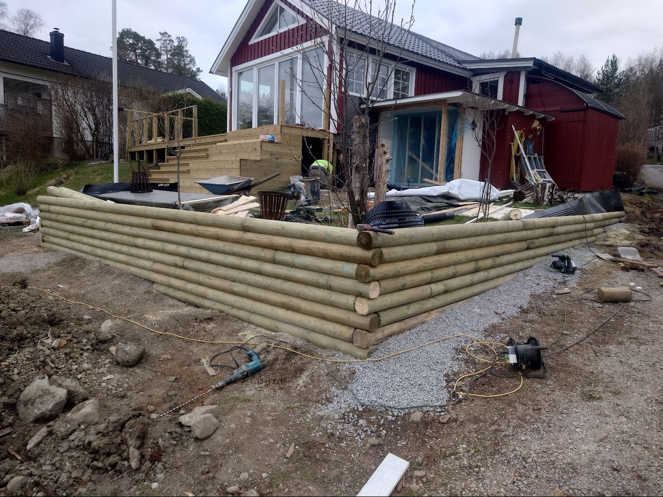 Budowa tarasu z drewnianą palisadą zabezpieczającą ziemię, widoczne narzędzia i materiały budowlane na placu budowy.