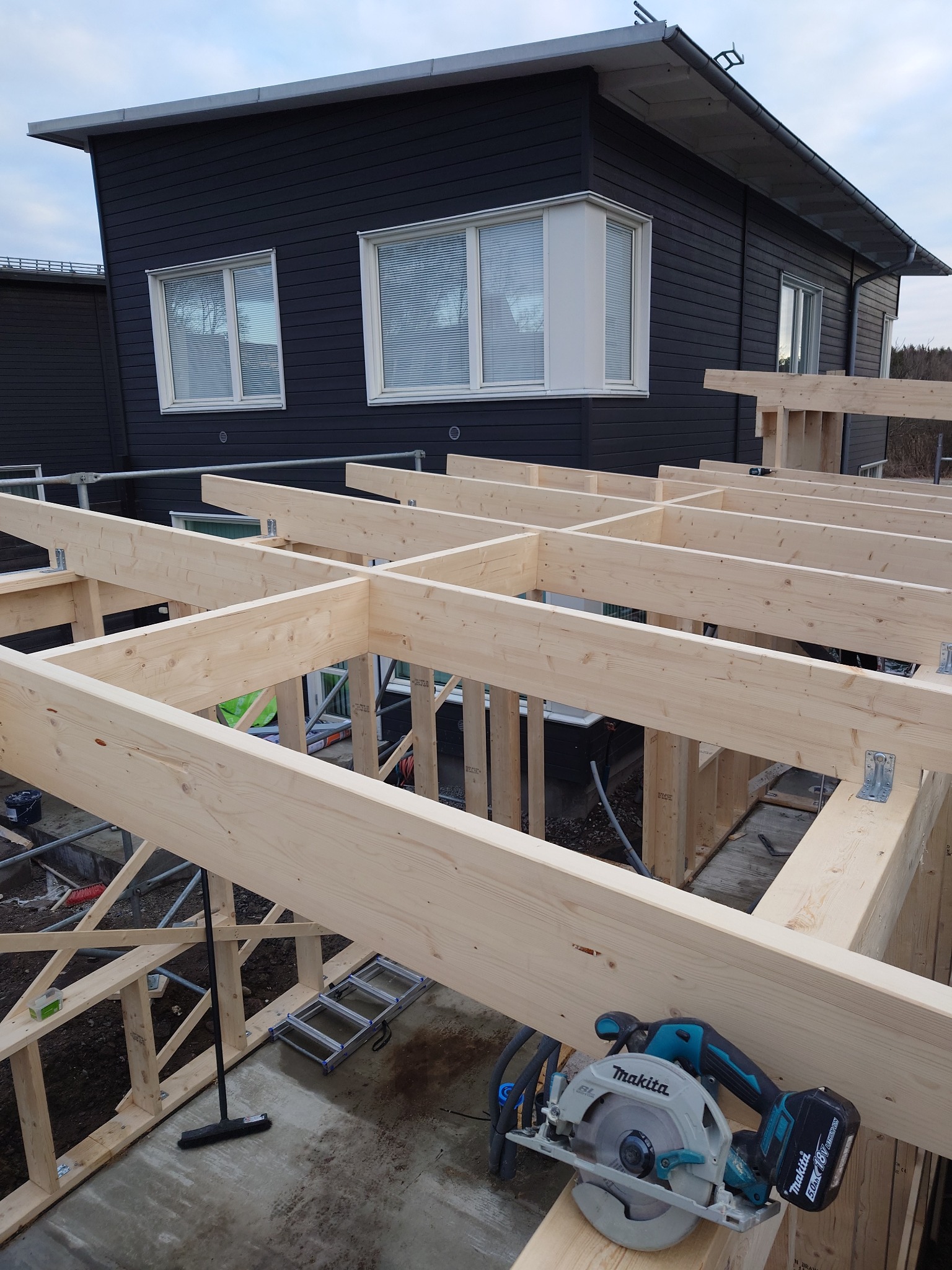 Konstrukcja drewniana domu szkieletowego w trakcie budowy, widoczna piła tarczowa Makita, czarne deski elewacyjne w tle.