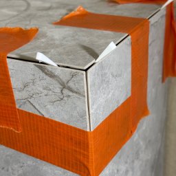 Tomasz Wojciechowski - Wykończona obudowa z płytek imitujących marmur, zabezpieczona pomarańczową taśmą i białymi krzyżykami dystansowymi, detale wykończenia.