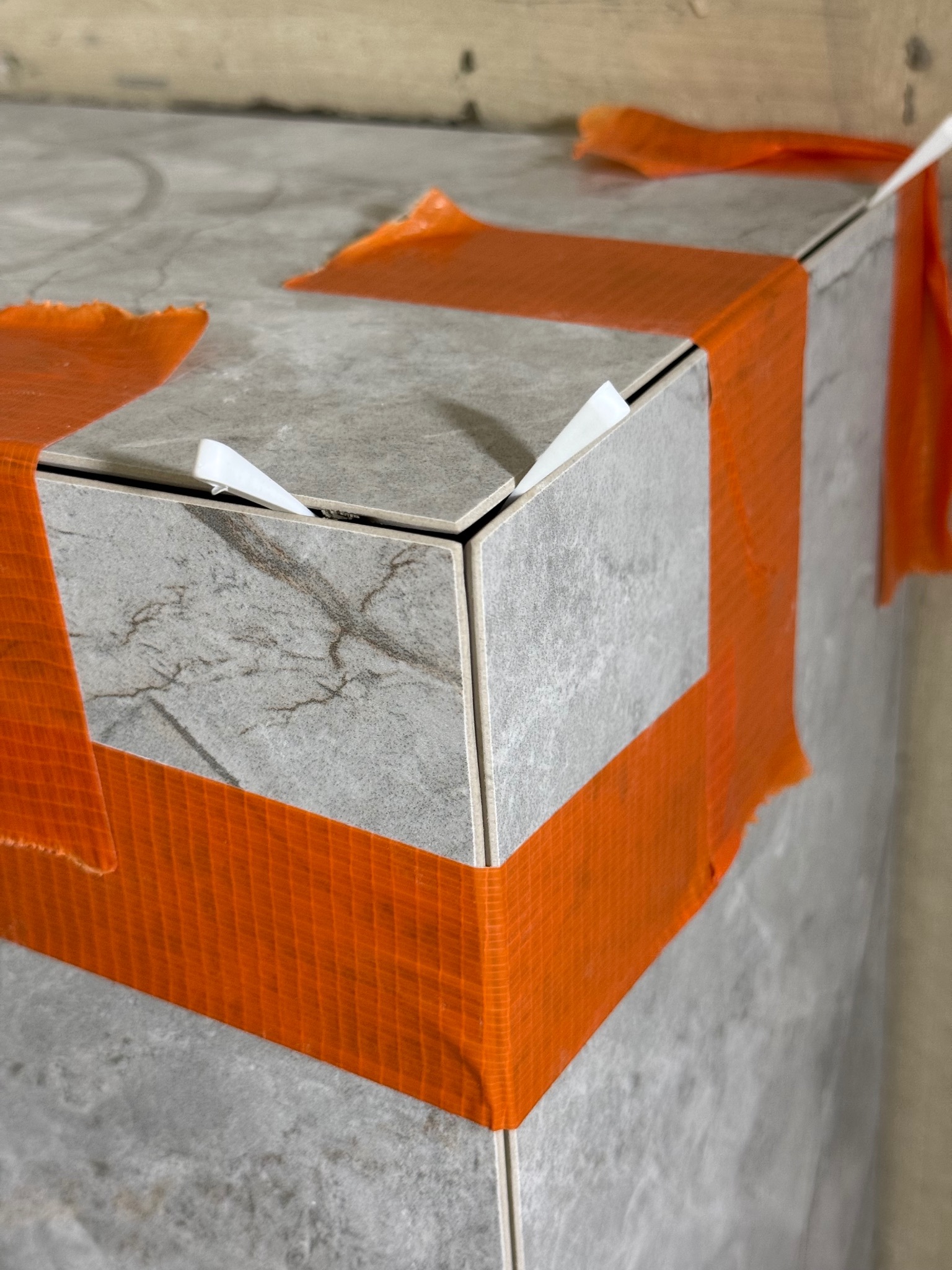 Wykończona obudowa z płytek imitujących marmur, zabezpieczona pomarańczową taśmą i białymi krzyżykami dystansowymi, detale wykończenia.