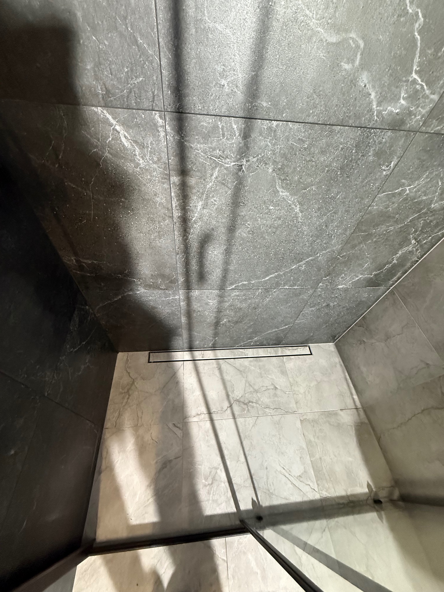 Nowoczesna kabina prysznicowa z szarymi płytkami imitującymi marmur, z odpływem liniowym. Minimalistyczny design, eleganckie wykończenie. Ujęcie z góry.