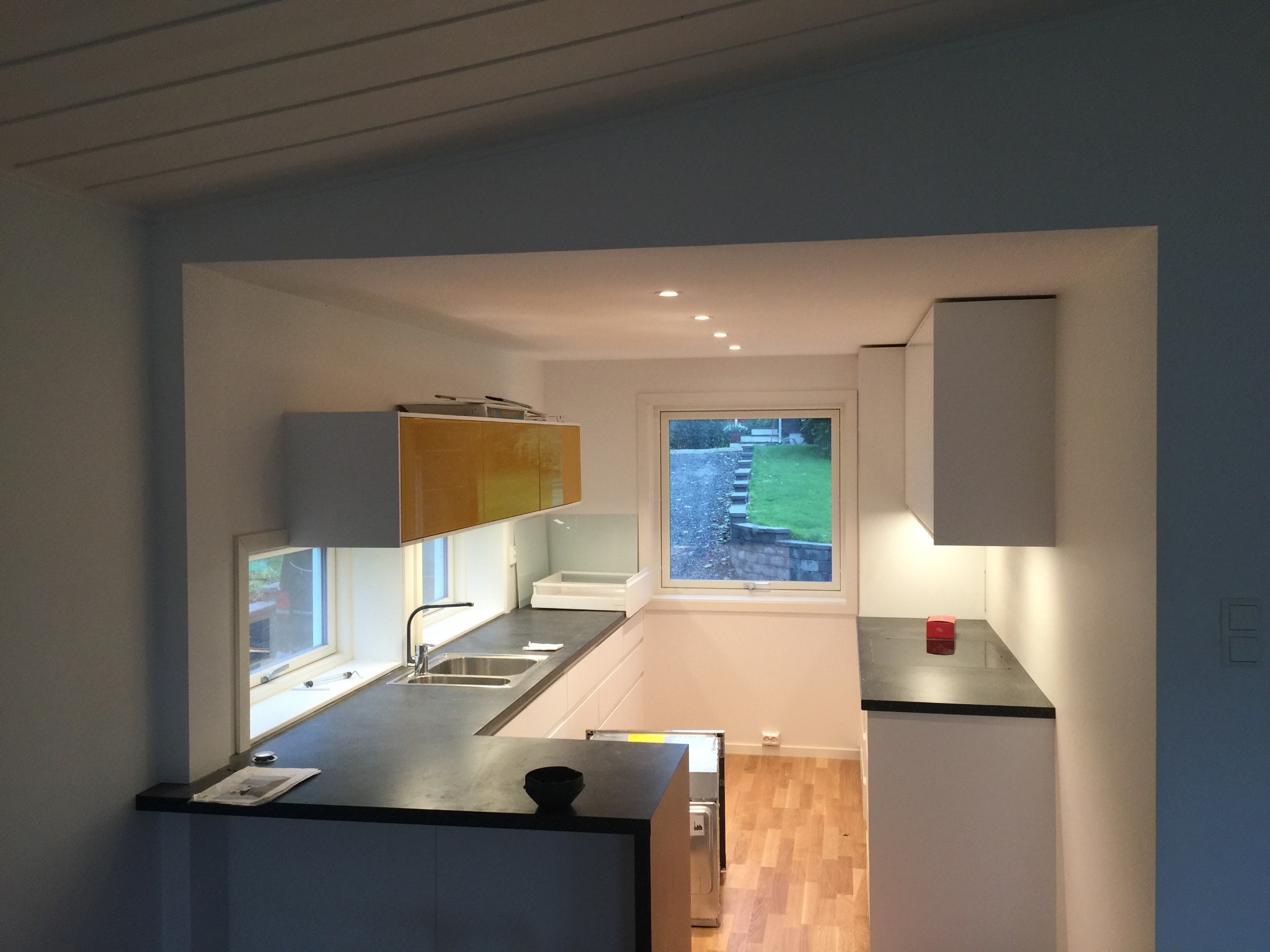 Nowoczesna kuchnia z oknami w Lublinie, z drewnianą podłogą i czarnym blatem, widok na ogród przez okno.