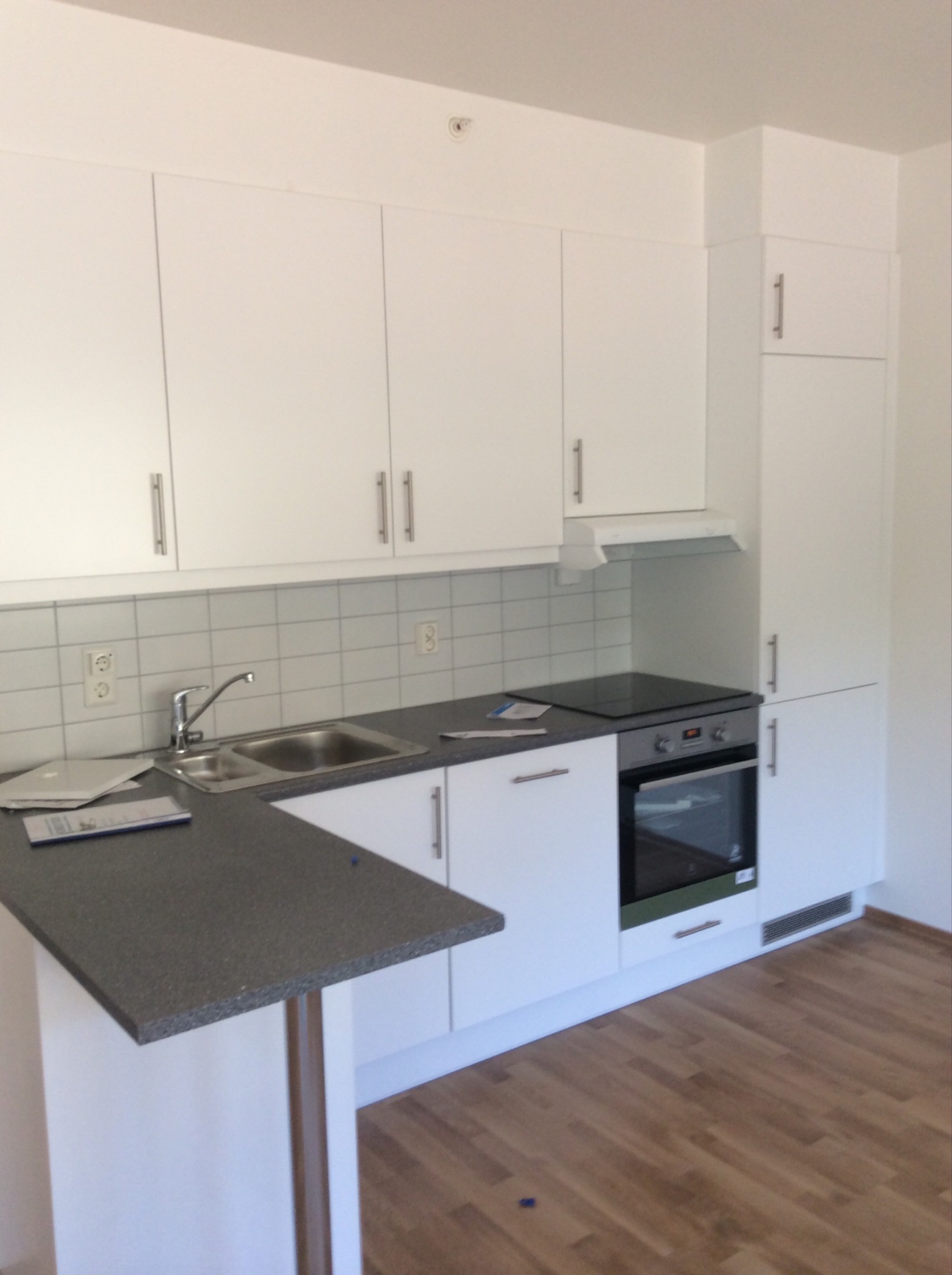 Nowoczesna, biała zabudowa kuchenna z szarą wyspą i drewnianą podłogą. Widoczne dokumenty na blacie.