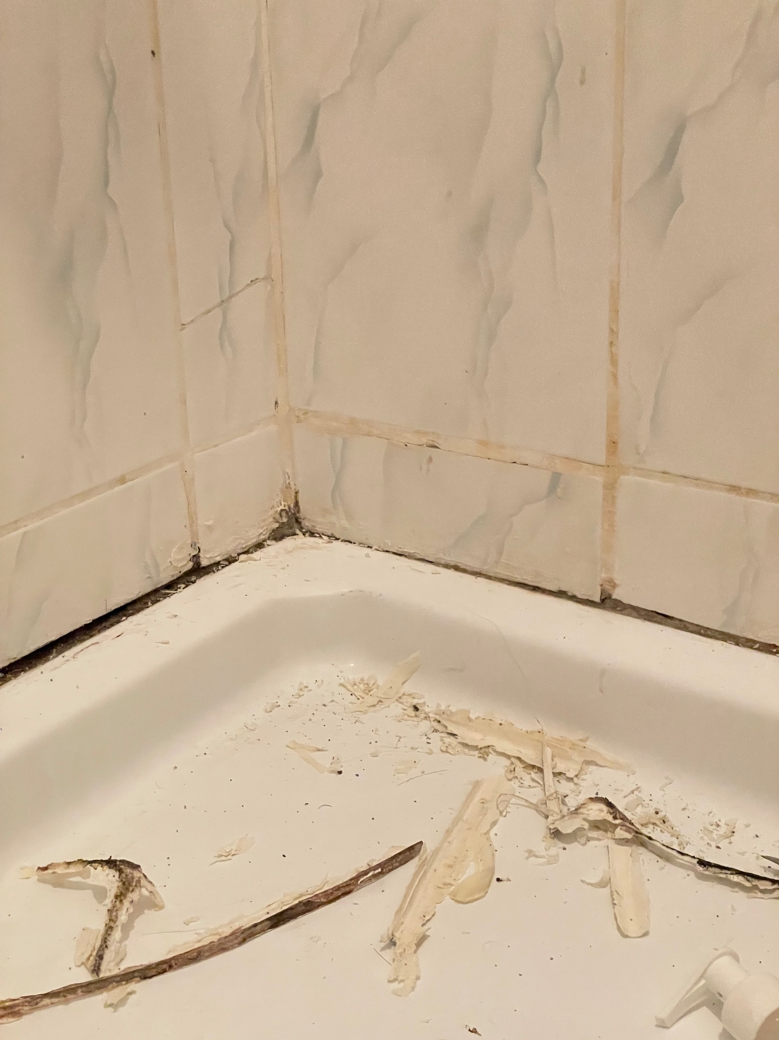 Fragment łazienki w trakcie usuwania starej fugi z płytek, widoczne resztki materiału i narzędzia na dnie brodzika.