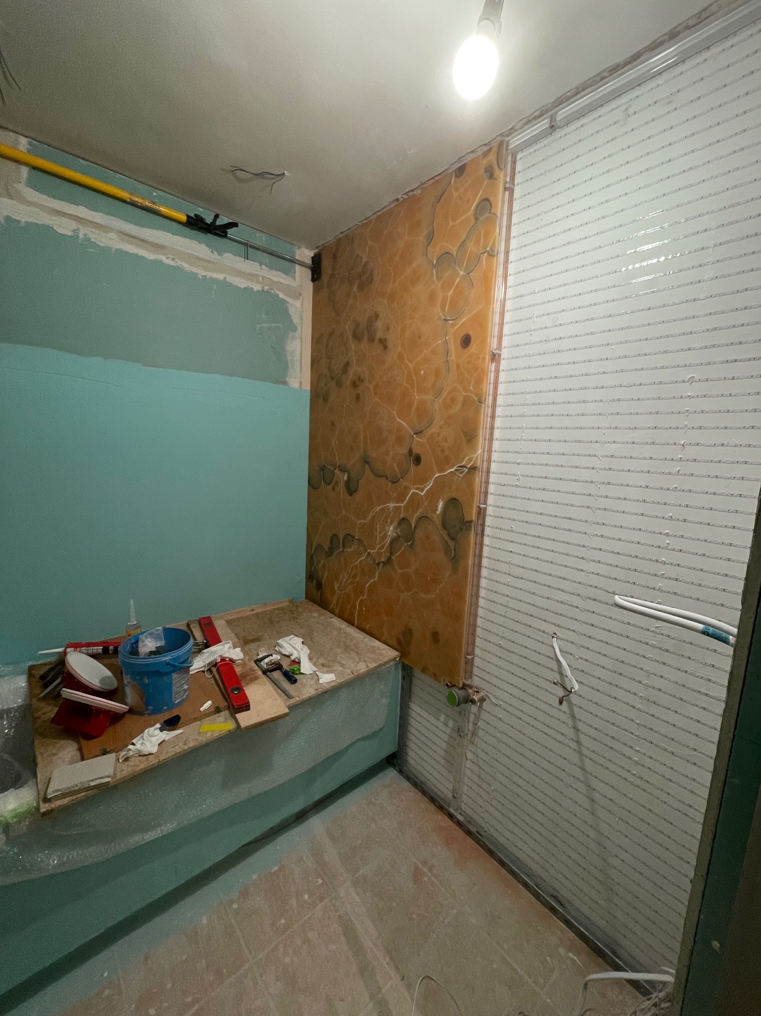 Wnętrze łazienki w trakcie prac: częściowo pomalowane ściany na turkusowo, okładzina z onyksu obok pionowych listew, widoczne narzędzia i materiały budowlane na prowizorycznym blacie.