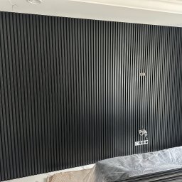 🏠 REMONTY & WYKOŃCZENIA WNĘTRZ 🏠 Jacek Sońta - Ściana wykończona czarnymi panelami lamelowymi, gniazdka elektryczne na ścianie, elementy instalacji elektrycznej widoczne, panele zabezpieczone folią.