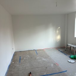 🏠 REMONTY & WYKOŃCZENIA WNĘTRZ 🏠 Jacek Sońta - Przygotowane do malowania wnętrze pokoju z zabezpieczonymi taśmą podłogami i listwami, widoczny wałek malarski i drabina.