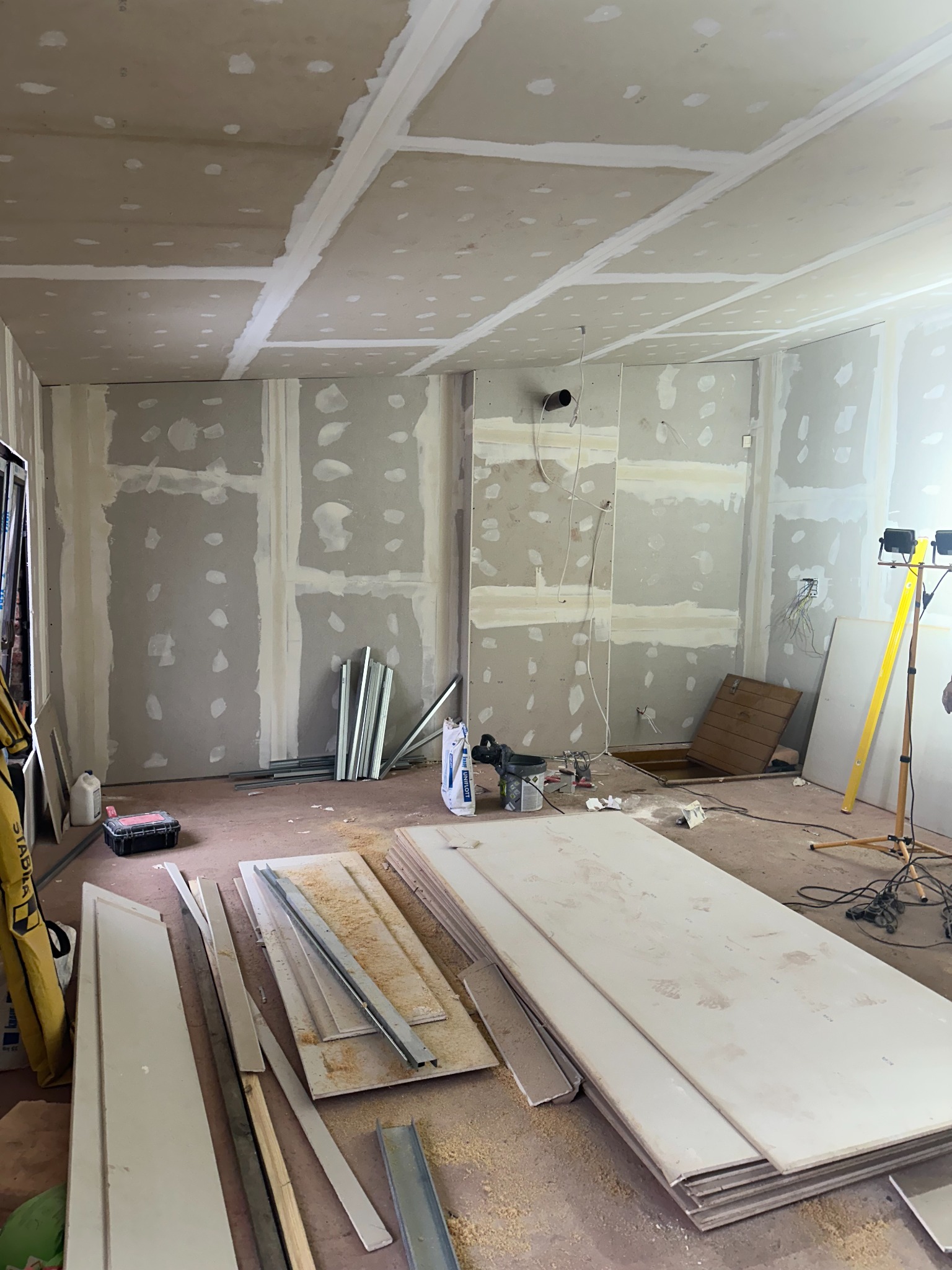 Wnętrze w trakcie prac: ściany i sufit pokryte płytami, widoczne profile, narzędzia i materiały budowlane, przygotowane do dalszych prac wykończeniowych.