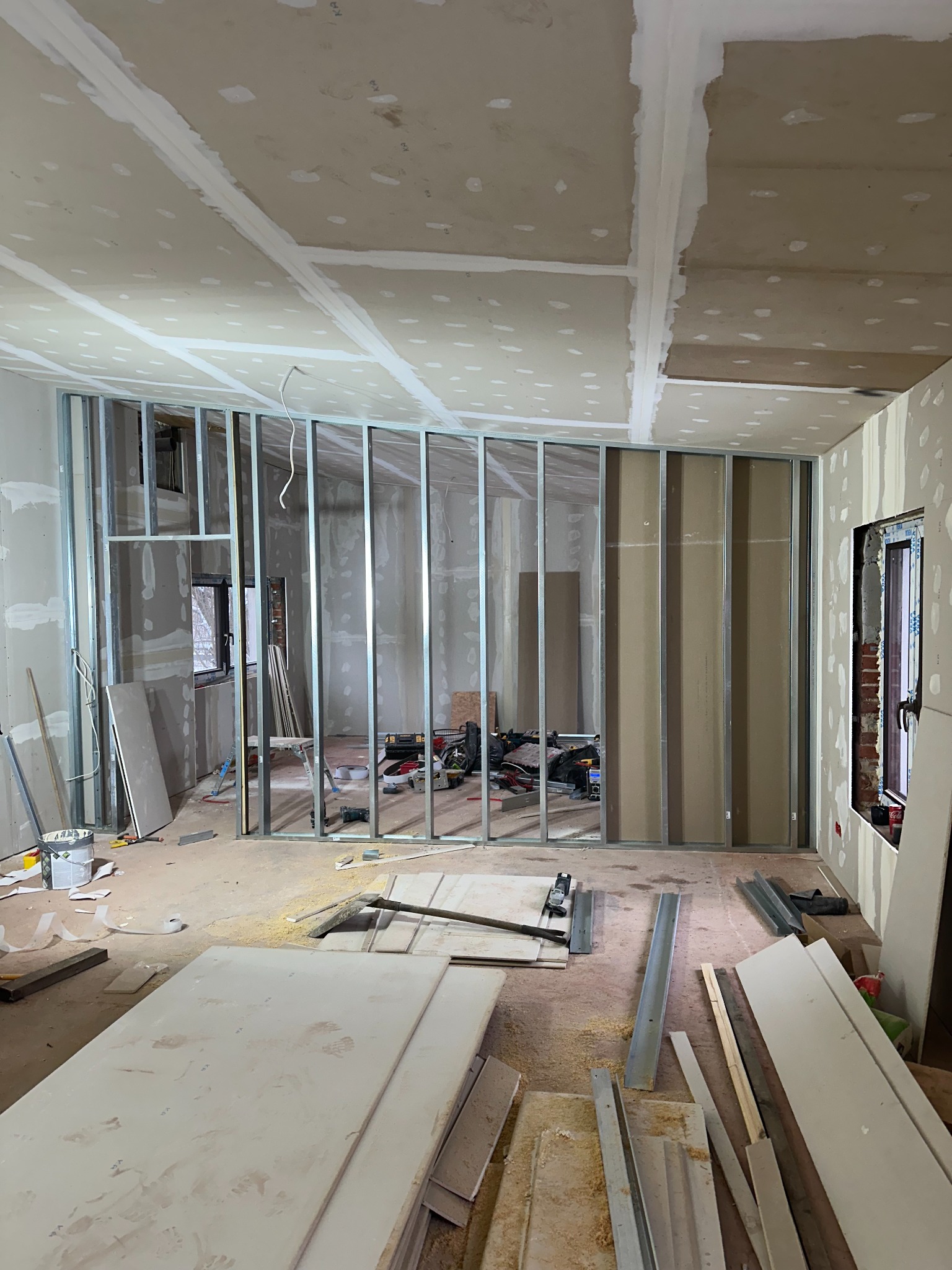 Wnętrze w trakcie montażu ścian działowych z metalowych profili i płyt. Widoczne narzędzia, profile, płyty i wstępnie wykończona sufitowa zabudowa.