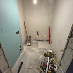 GRCZDR - Łazienka w trakcie remontu: ściany z płyt gipsowo-kartonowych, częściowo pokryte gładzią, instalacja wodna i elektryczna widoczna, liczne narzędzia i materiały budowlane na podłodze.