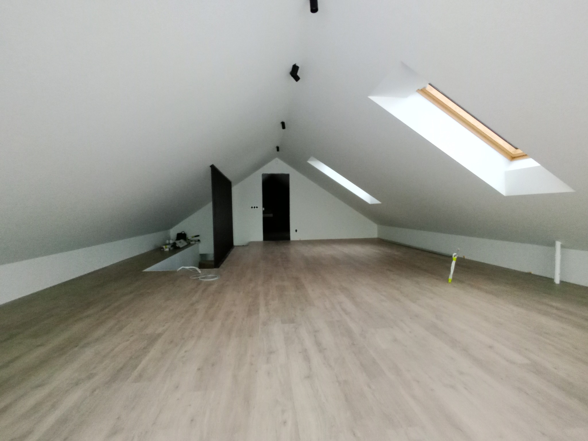 Jasne panele podłogowe w nowym poddaszu z oknami dachowymi i widocznym oświetleniem punktowym. Minimalistyczny design, świeżo po remoncie.