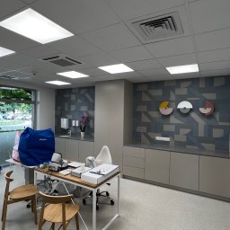 Majster Jakości - Ihor Kondrashov - Wnętrze biura z geometrycznym wzorem na ścianie, jasne meble, drewniane krzesła i nowoczesne oświetlenie sufitowe.