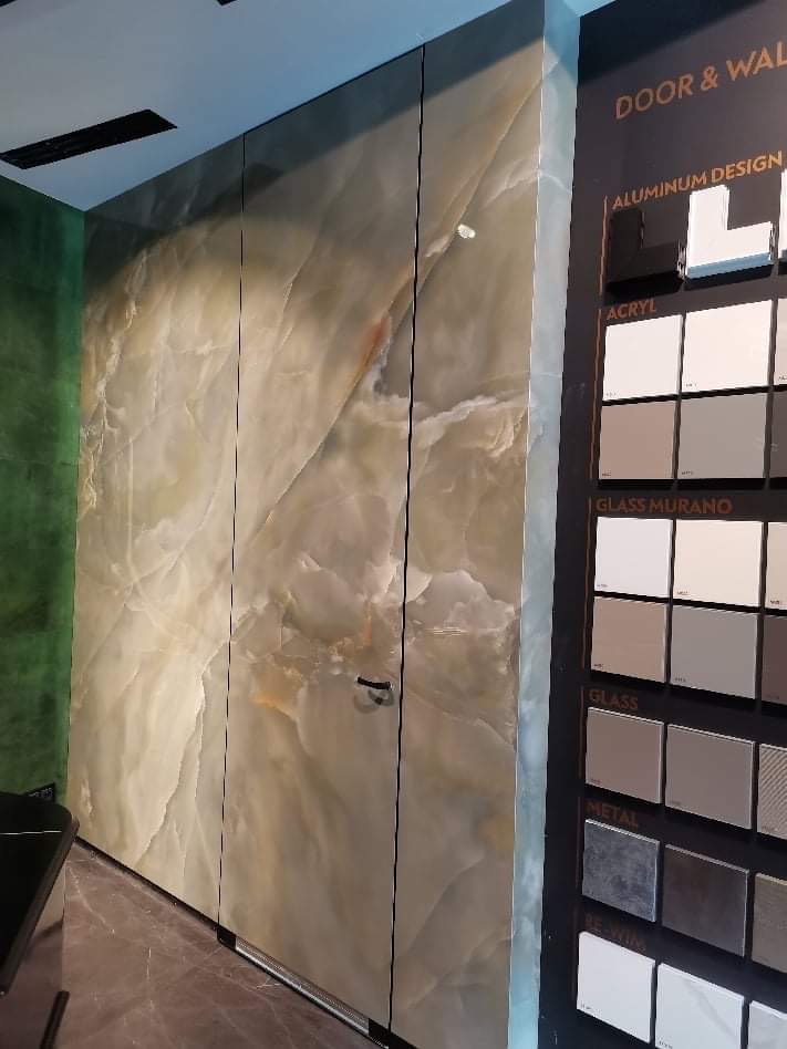 Ściana wykończona płytami imitującymi marmur, z uchwytem, obok ekspozytor z próbkami materiałów wykończeniowych.