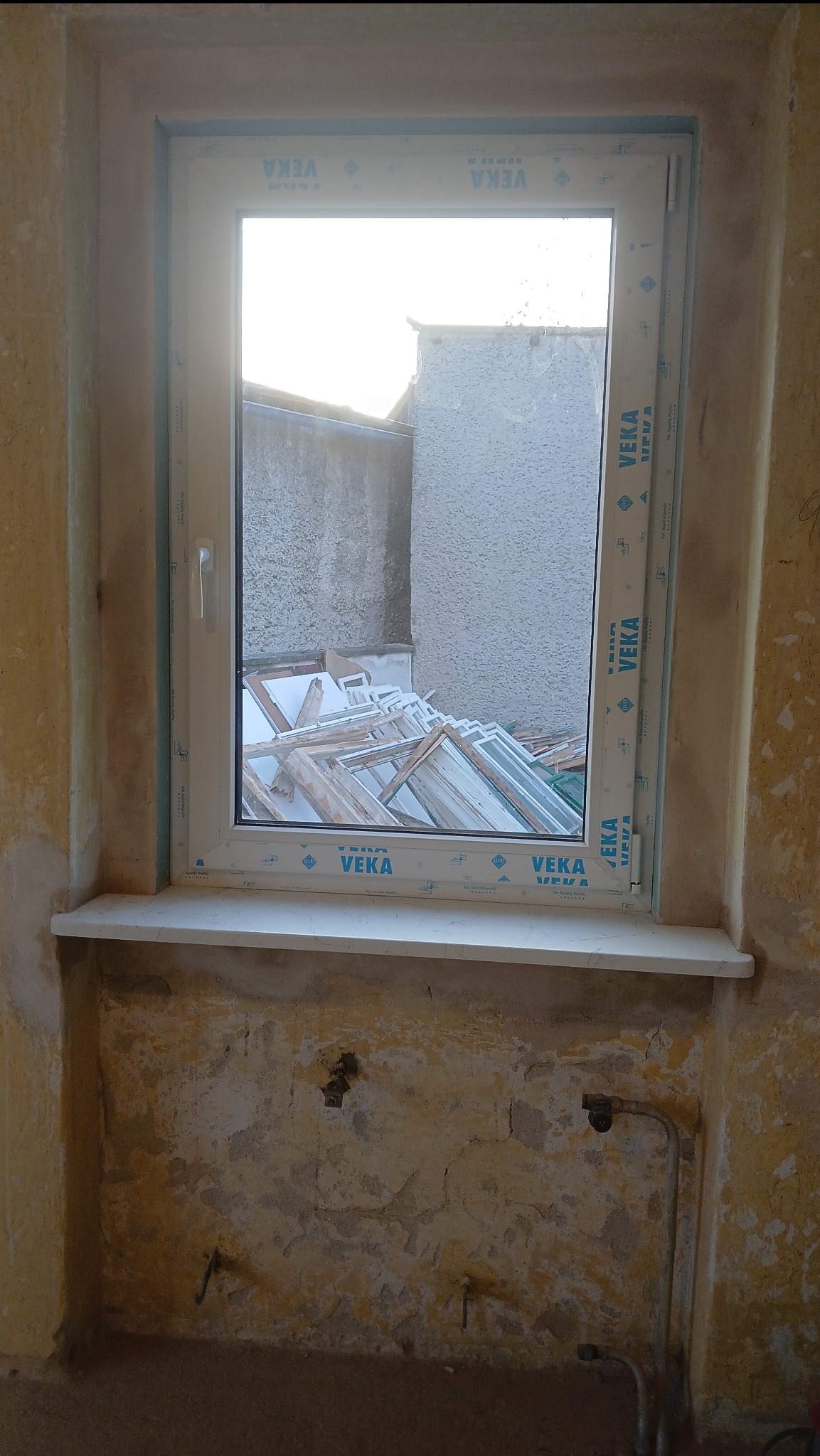 Zamontowane okno PCV marki VEKA w Katowicach, widok na podwórze z oknami do wymiany. Ściany w trakcie remontu, widoczne ślady po instalacjach.