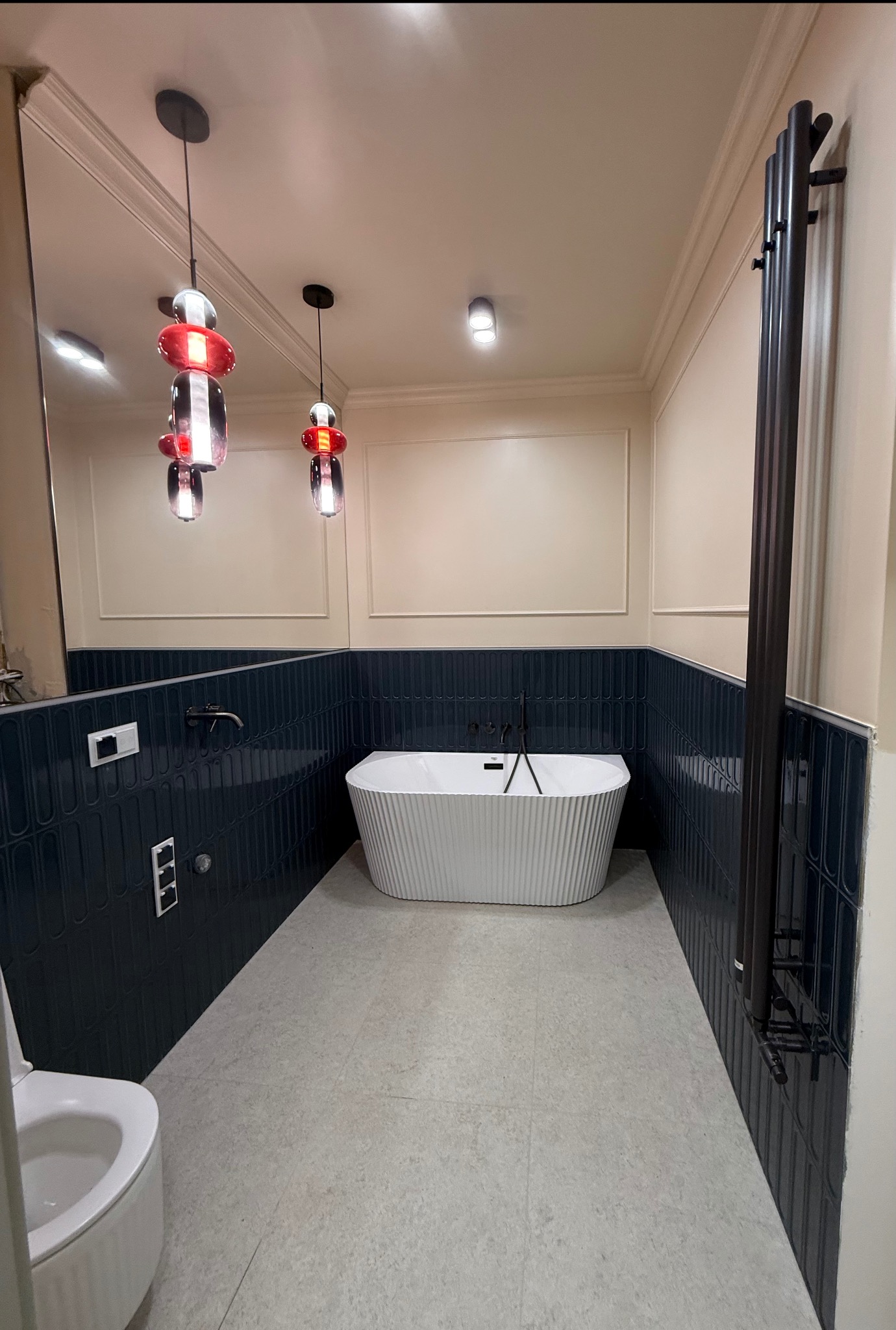 Nowoczesna łazienka z wanną wolnostojącą, ciemnymi płytkami i designerskimi lampami wiszącymi. Uwagę zwraca grzejnik drabinkowy i minimalistyczna armatura.