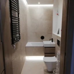 Nowoczesna łazienka z beżowymi płytkami imitującymi marmur, podświetleniem LED pod wanną i nad lustrem, wiszącą toaletą i grzejnikiem drabinkowym w kolorze czarnym.