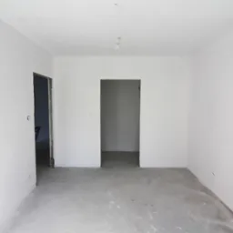 Pusty pokój po remoncie, świeżo wygładzone i pomalowane ściany na biało, surowa podłoga, widoczne dwa otwory drzwiowe.