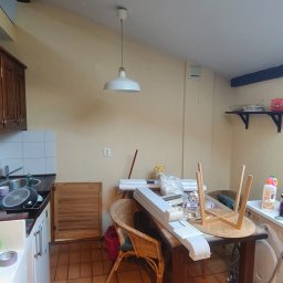 Tomasz Pawlik - Wnętrze kuchni w trakcie remontu: widoczne przygotowania do prac wykończeniowych, materiały budowlane na stole, ściany w jasnym odcieniu przed malowaniem.