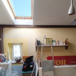 Tomasz Pawlik - Wnętrze pokoju w trakcie odświeżania: ściany w odcieniach beżu, drabina malarska, okno dachowe i widoczne ślady prac remontowych. Częściowo pomalowana ściana.