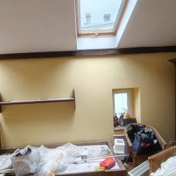 Tomasz Pawlik - Pokój przed remontem: żółte ściany, drewniane belki stropowe, okno dachowe, meble i akcesoria przygotowane do zabezpieczenia przed pracami remontowymi.