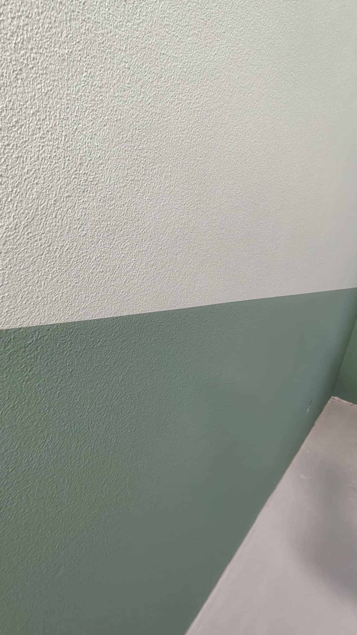 Pomieszczenie po malowaniu: górna część ściany biała z fakturą, dolna część zielona. Widoczny fragment podłogi. Ściana pomalowana do połowy.