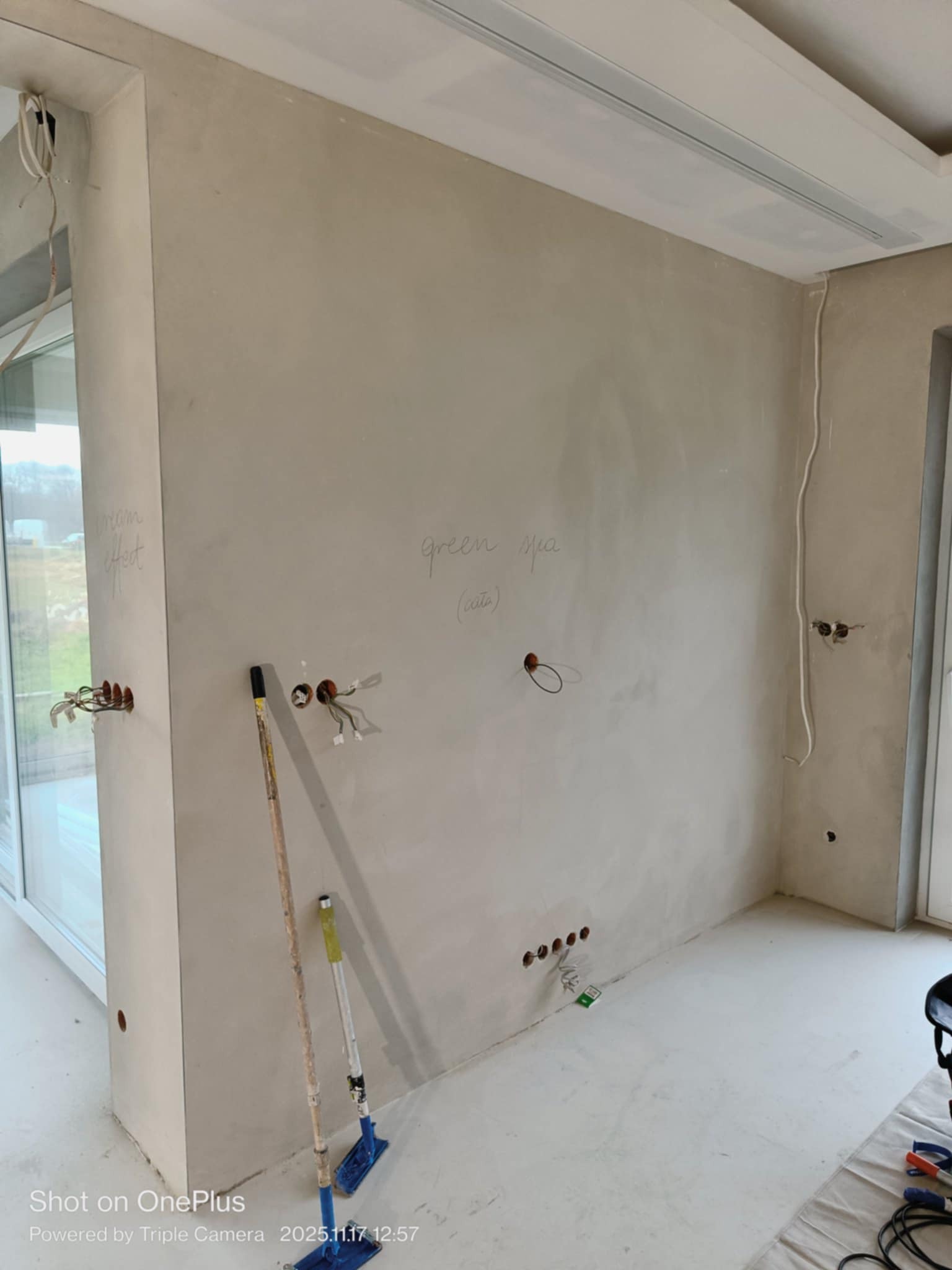 Ściana po szpachlowaniu z napisem 'green sea' i 'cream effect', widoczne puszki elektryczne i narzędzia malarskie. Przygotowanie do malowania.