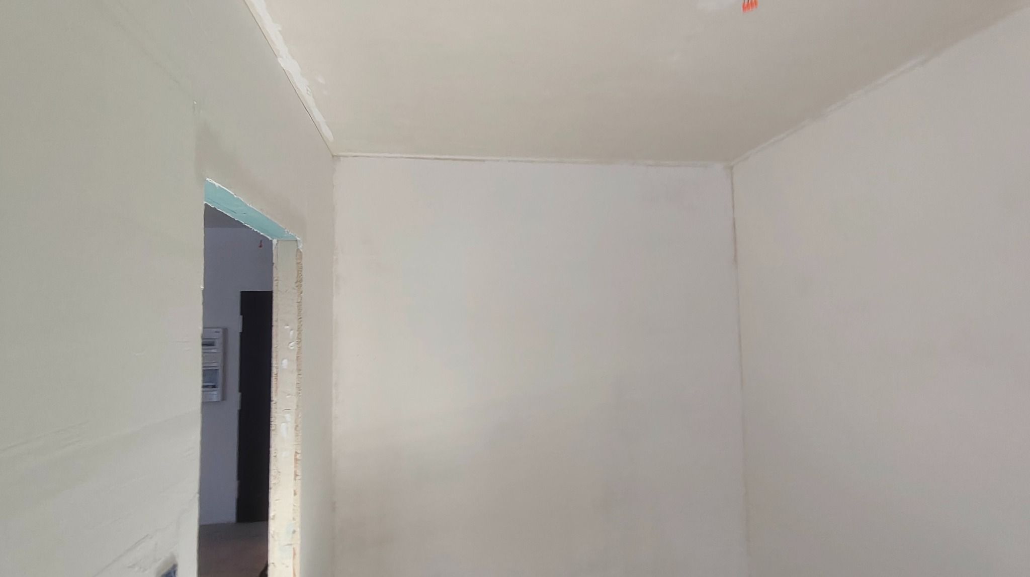 Wnętrze pokoju po szpachlowaniu ścian i sufitu, widoczne gładkie powierzchnie przygotowane do malowania. W tle fragment ościeżnicy drzwiowej.