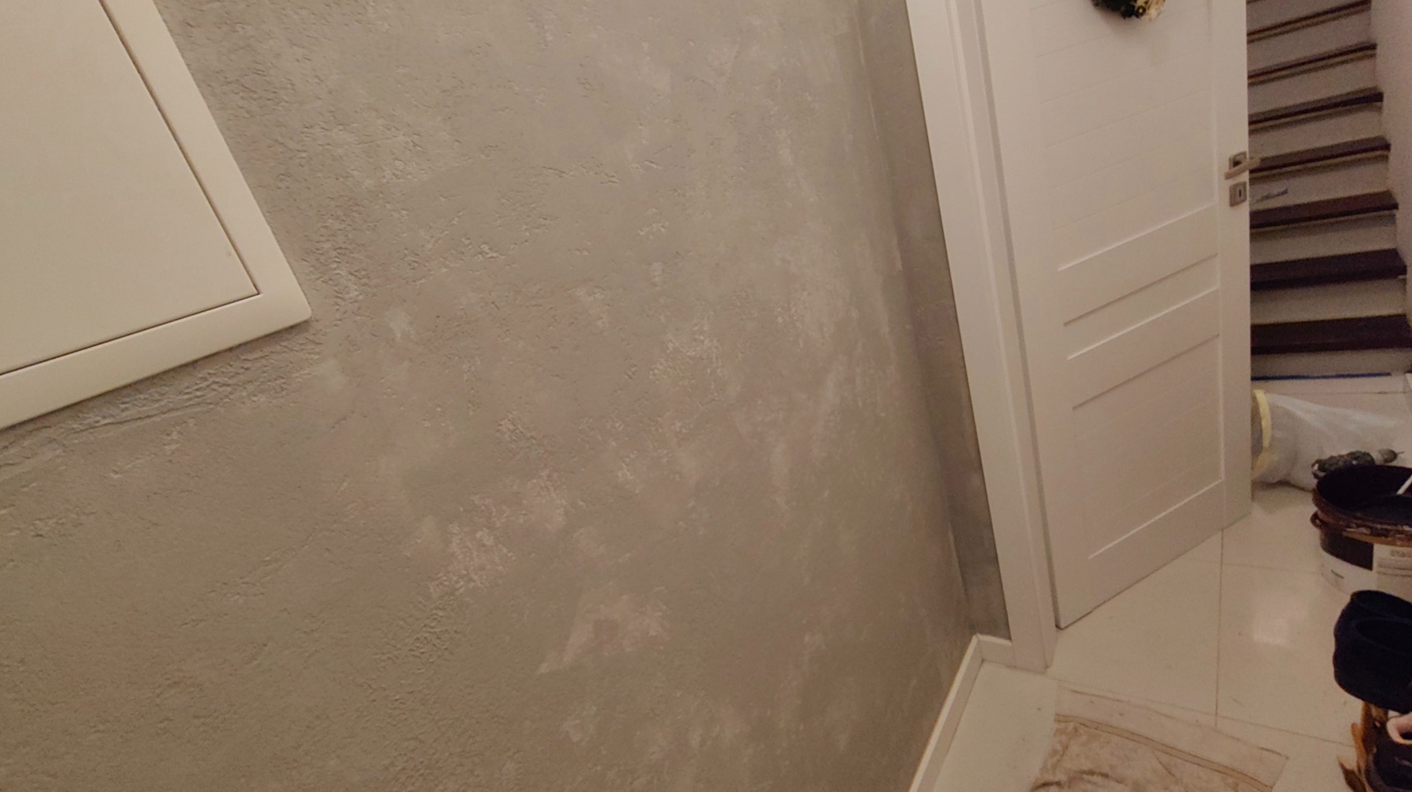 Ściana z efektem dekoracyjnym w odcieniach szarości, widoczna obok białych drzwi i klapy rewizyjnej. Tekstura ściany nieregularna, z subtelnymi przejściami tonalnymi.