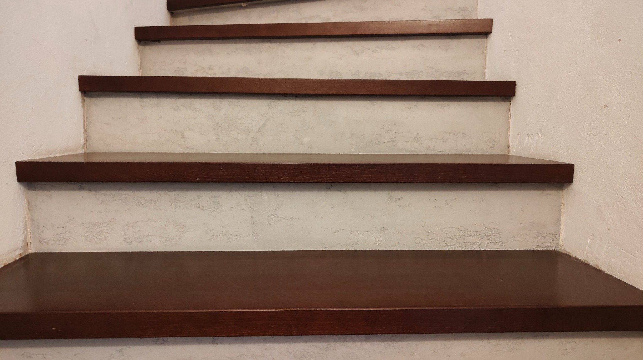 Schody z drewnianymi stopniami i ścianą pokrytą dekoracyjną, jasną strukturą. Widoczne detale wykończenia i faktura ściany.