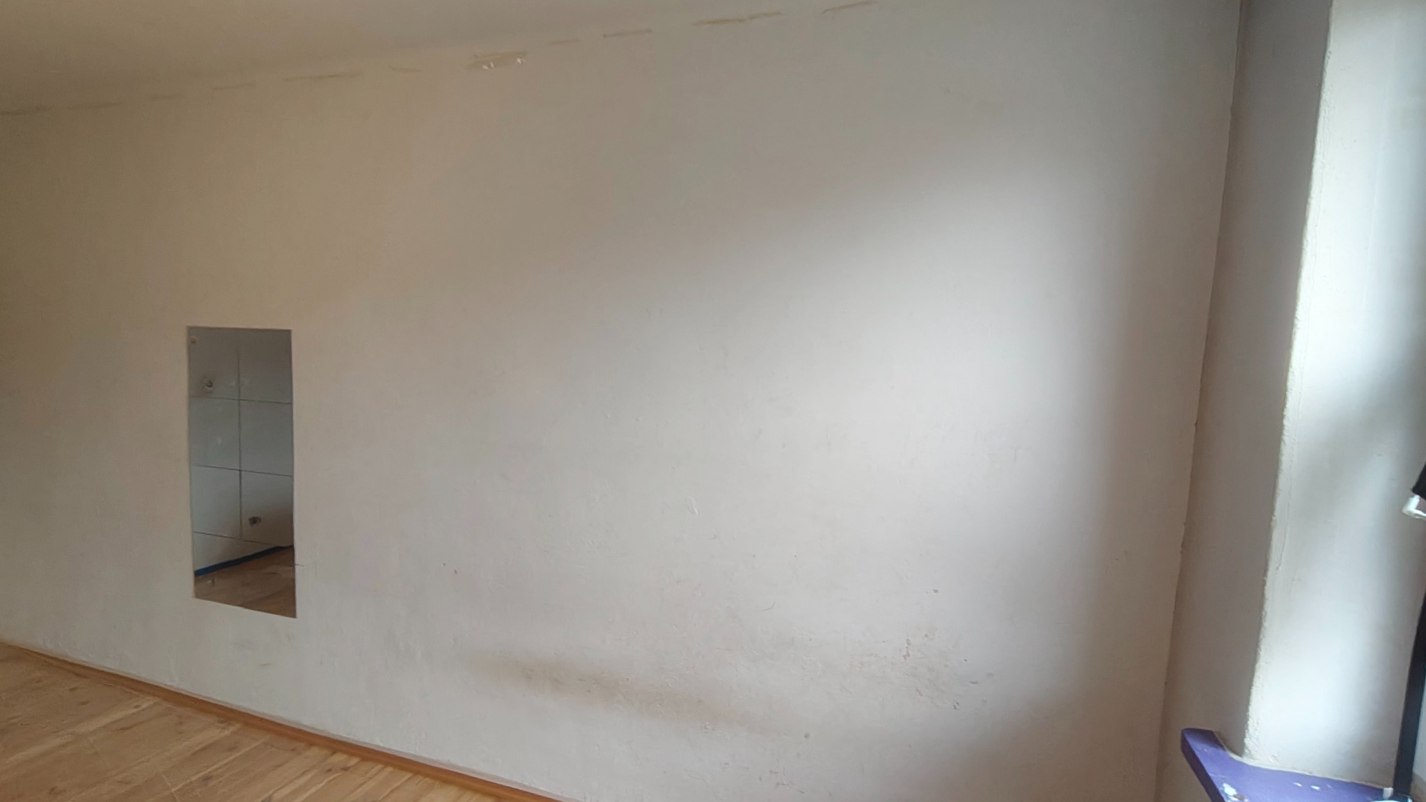 Ściana w pokoju przed malowaniem z widocznymi śladami po szpachlowaniu i otworze w ścianie. Parkiet na podłodze. Przygotowanie do prac wykończeniowych.