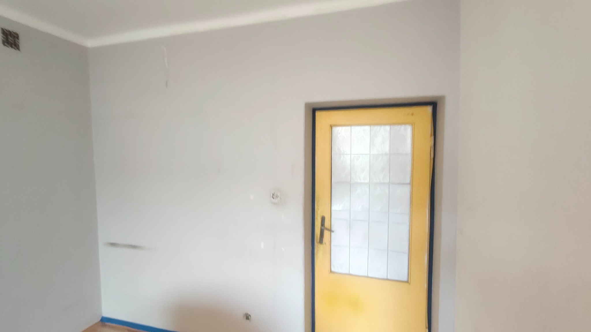 Wnętrze pokoju po odświeżeniu: szare ściany, żółte drzwi z szybami. Widoczne ślady po wcześniejszych pracach, przygotowane do dalszego wykończenia.