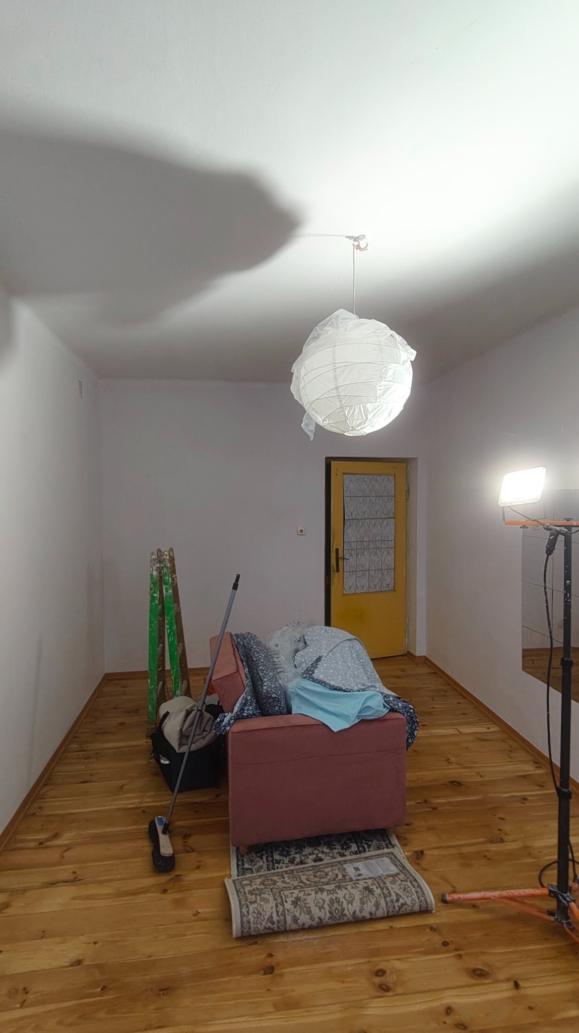 Pokój w trakcie przygotowań do prac wykończeniowych w Krakowie. Widoczne zabezpieczone meble, drabina i lampa oświetleniowa. Ściany przygotowane do malowania.