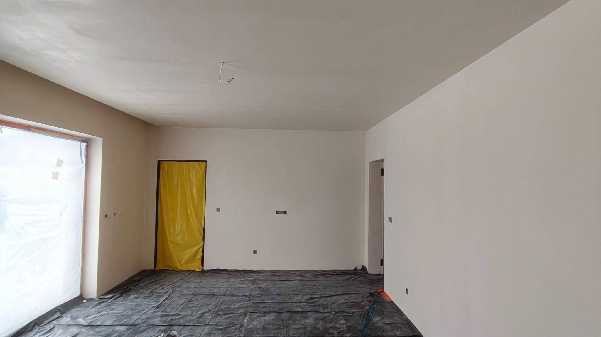 Wnętrze po szpachlowaniu: gładkie, białe ściany, zabezpieczona folią podłoga i drzwi. Przygotowanie do malowania natryskowego.