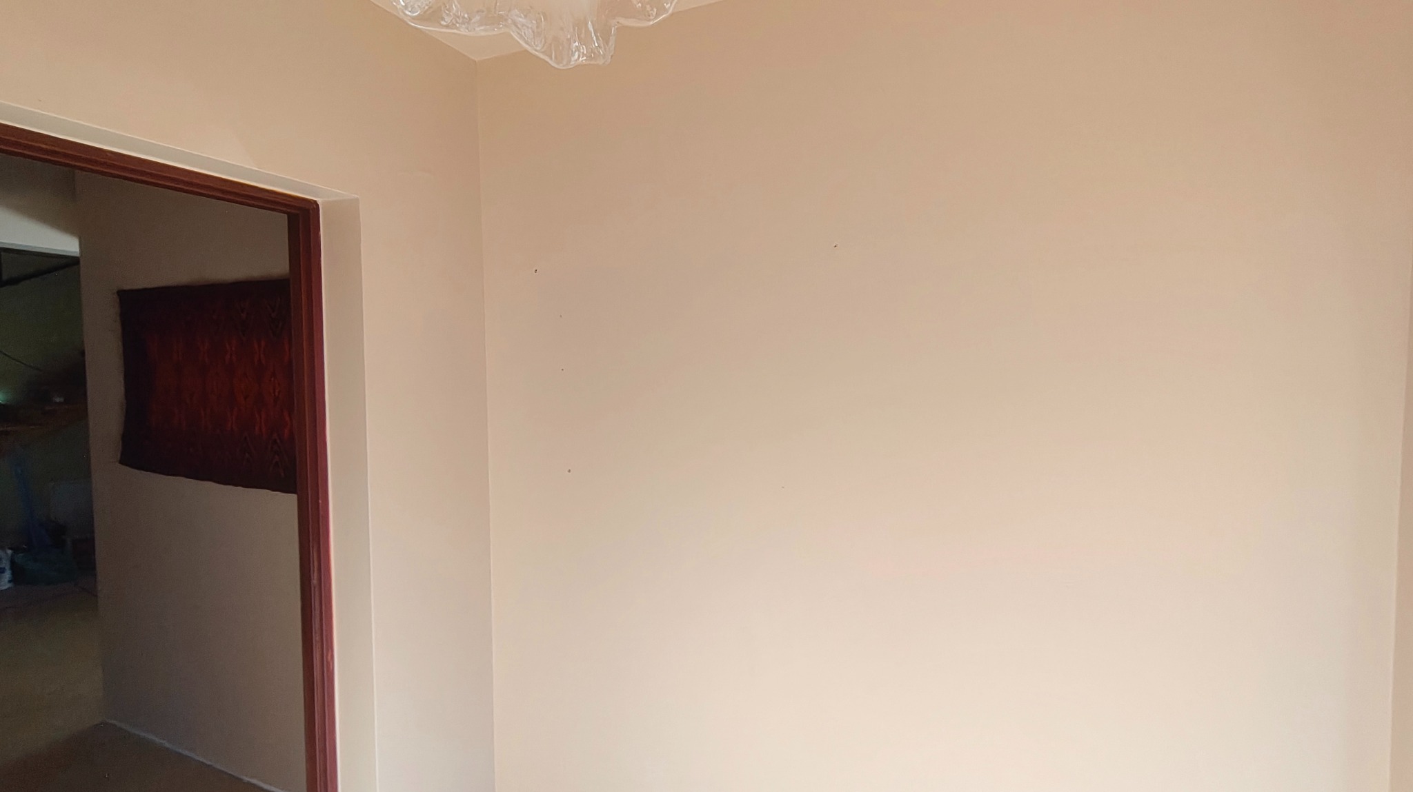 Jasna ściana po świeżym malowaniu, widoczne drobne niedoskonałości i fragment futryny drzwi. Na suficie folia ochronna.